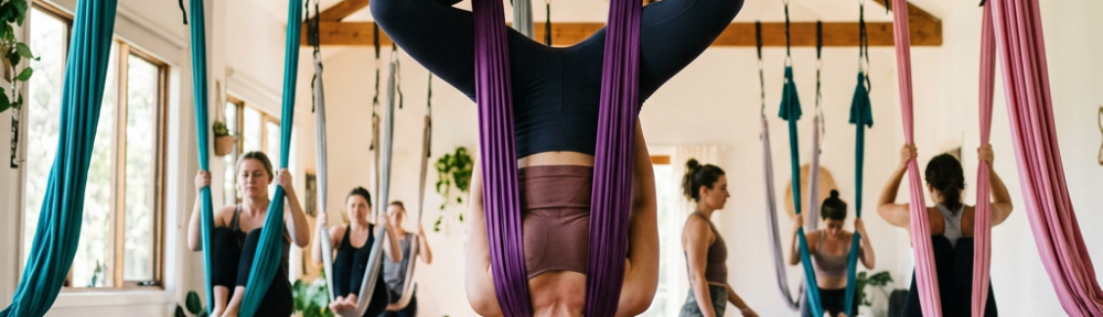 Group of people performing aerial yoga using suspended fabric hammocks in a brightly lit studio